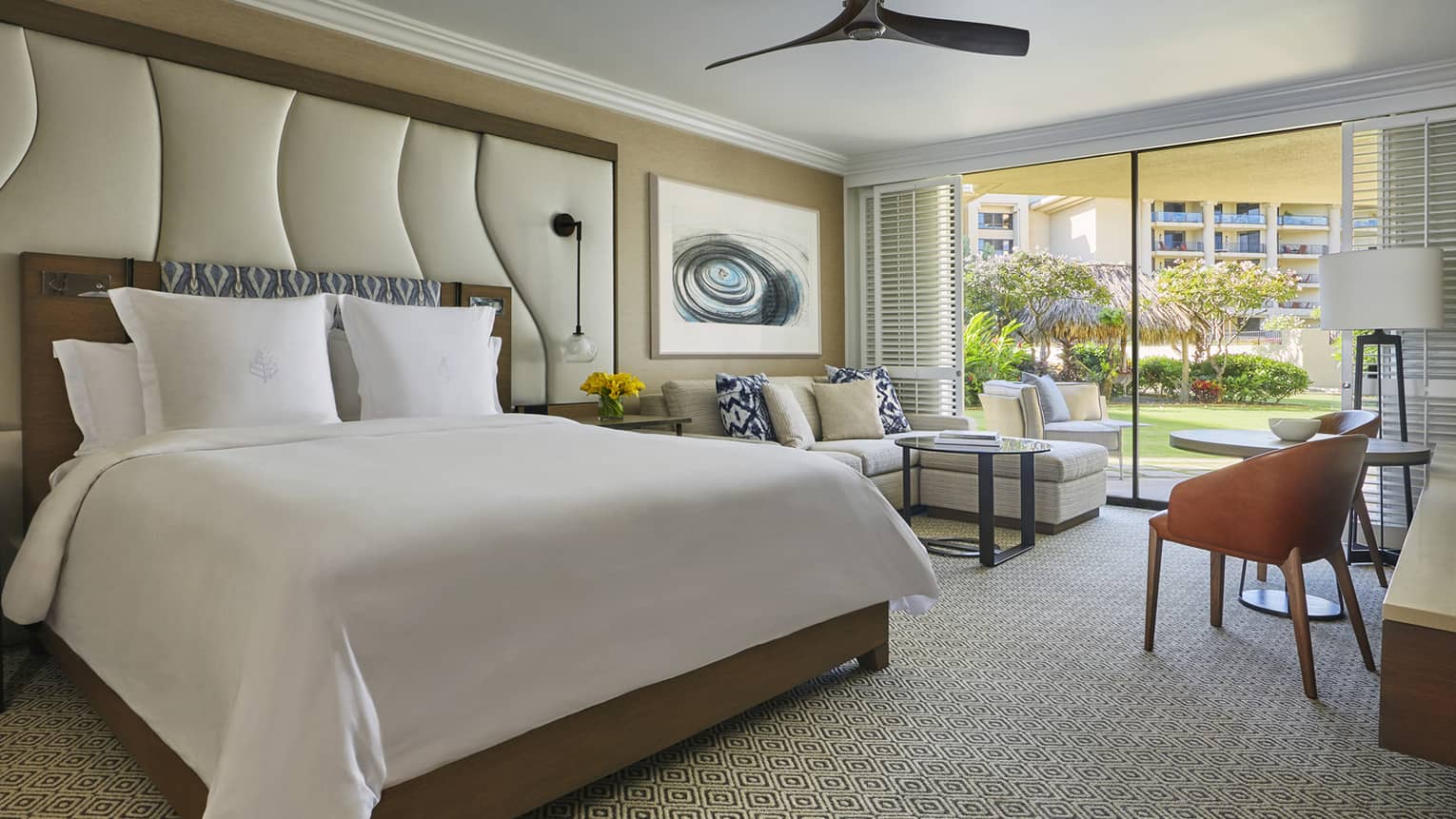 Guest room with king bed, seating area, desk and sliding doors opening to garden view and outdoor lounge chairs
