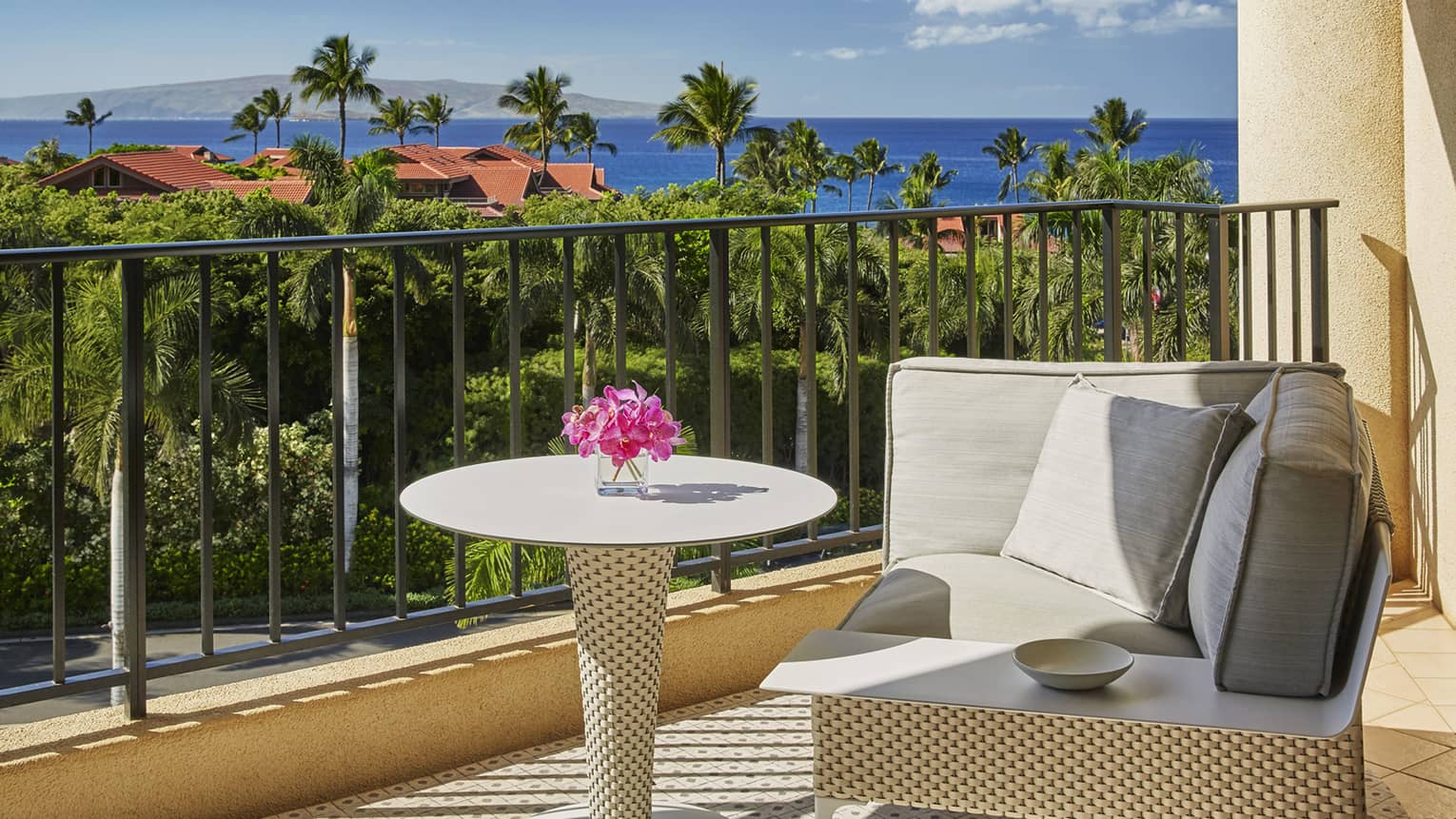 Beige wicker patio chair and table with pink tropical flower in vase on sunny balcony
