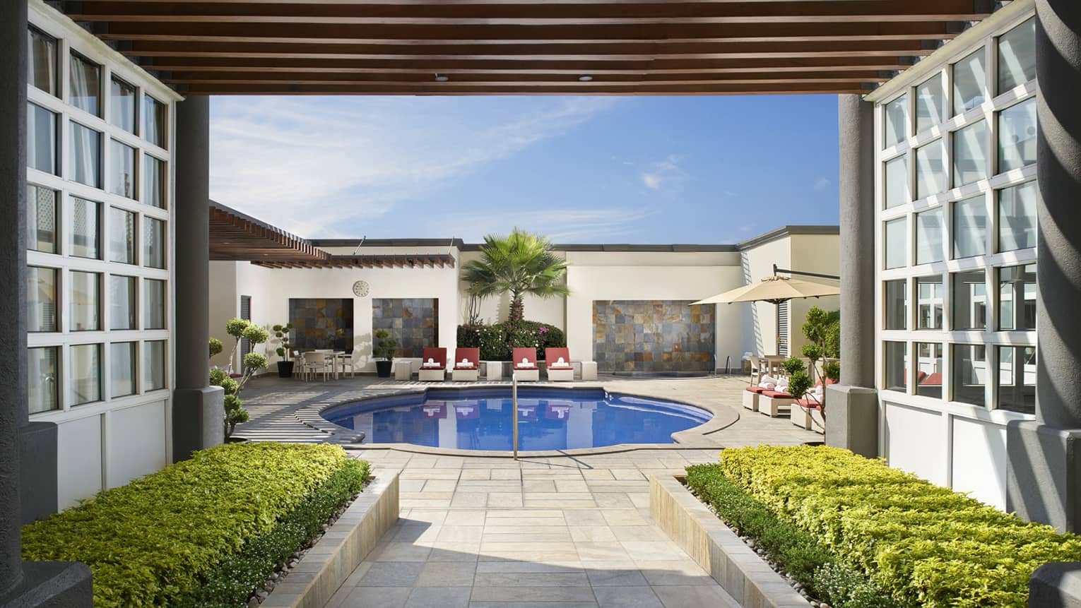 Walkway under awning leading to round blue swimming pool, lounge chairs on sunny deck