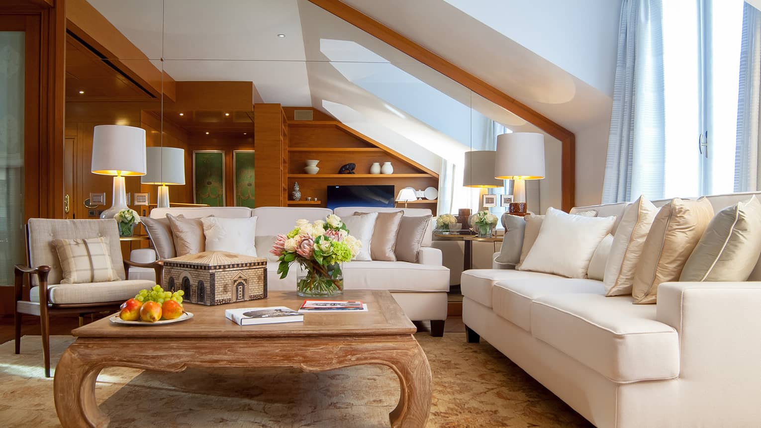 Living room with two white sofas around square wooden coffee table with fresh flowers and books