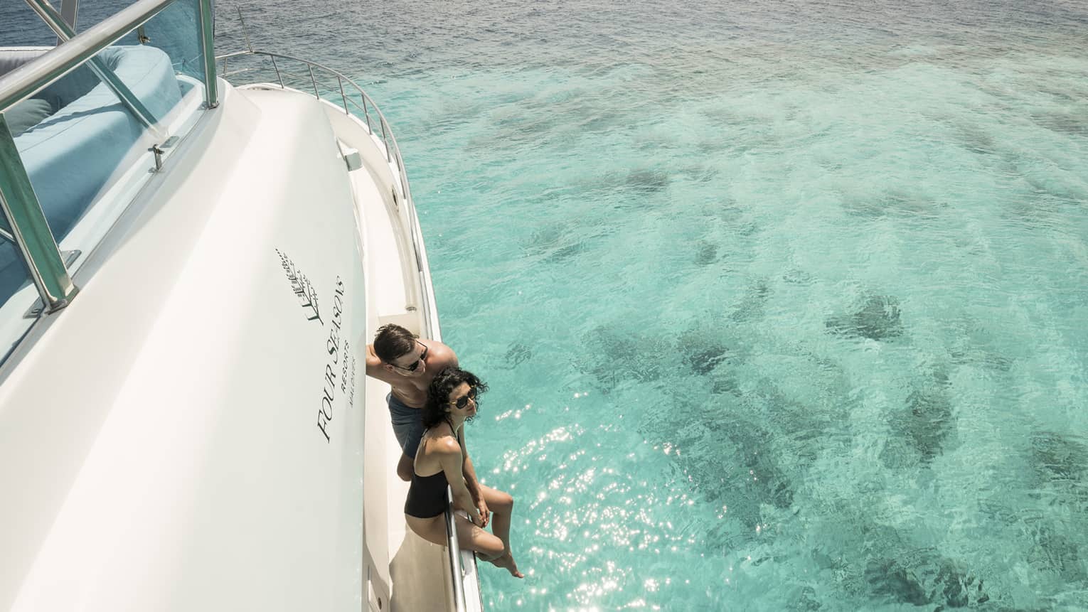 A couple lounges on the side of a yacht in a blue lagoon