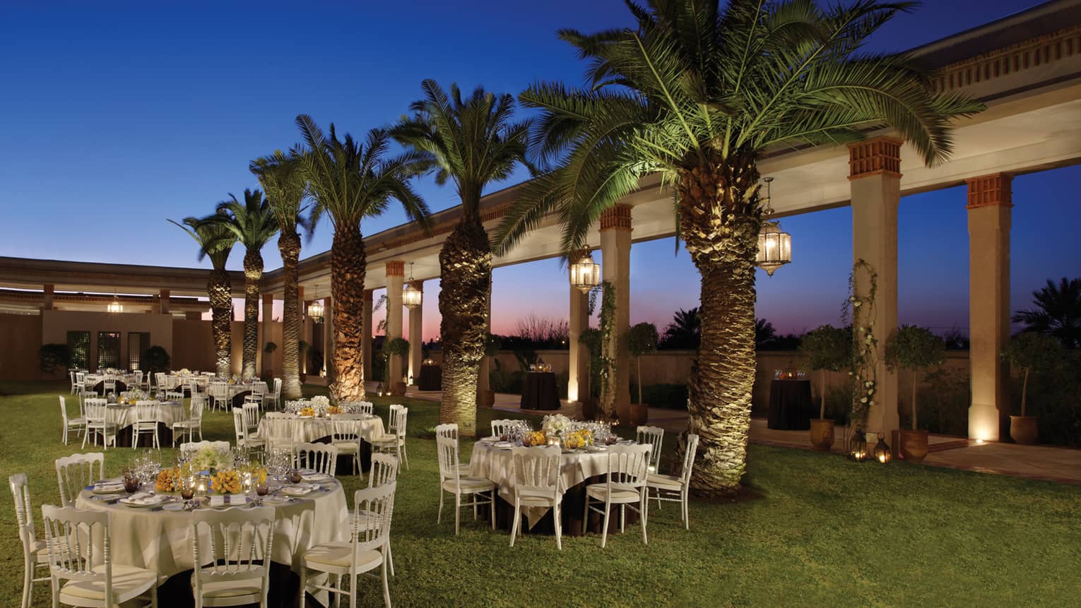 Le Jardin event lawn at night with small banquet tables, row of palm trees 
