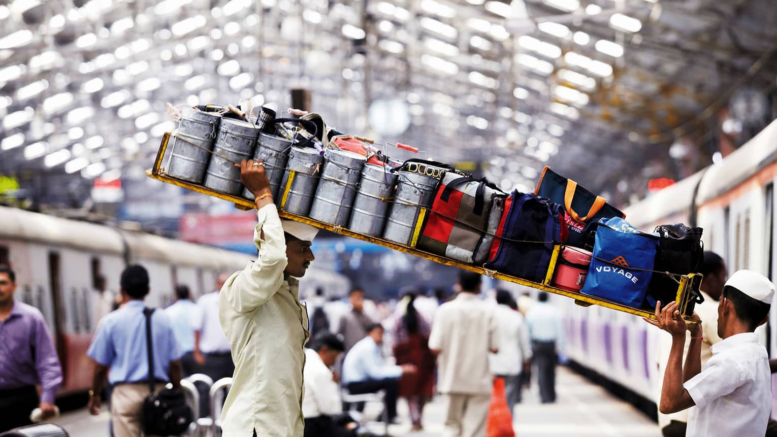 Dabbawalas lunchbox delivery men carry long tray with bags, cans through station