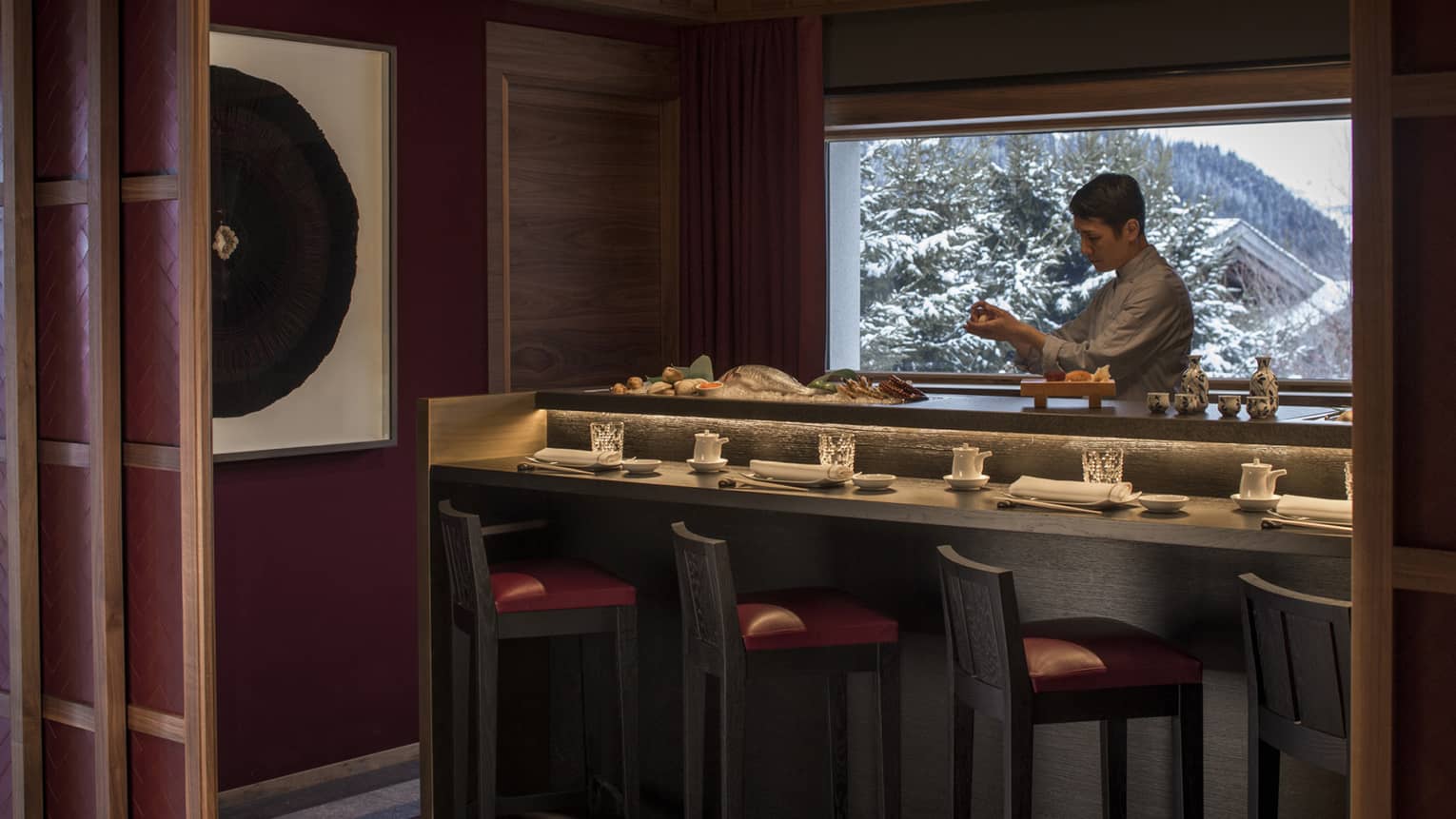 Kaito sushi chef at small bar with fresh whole fish, seafood, window with winter mountain views