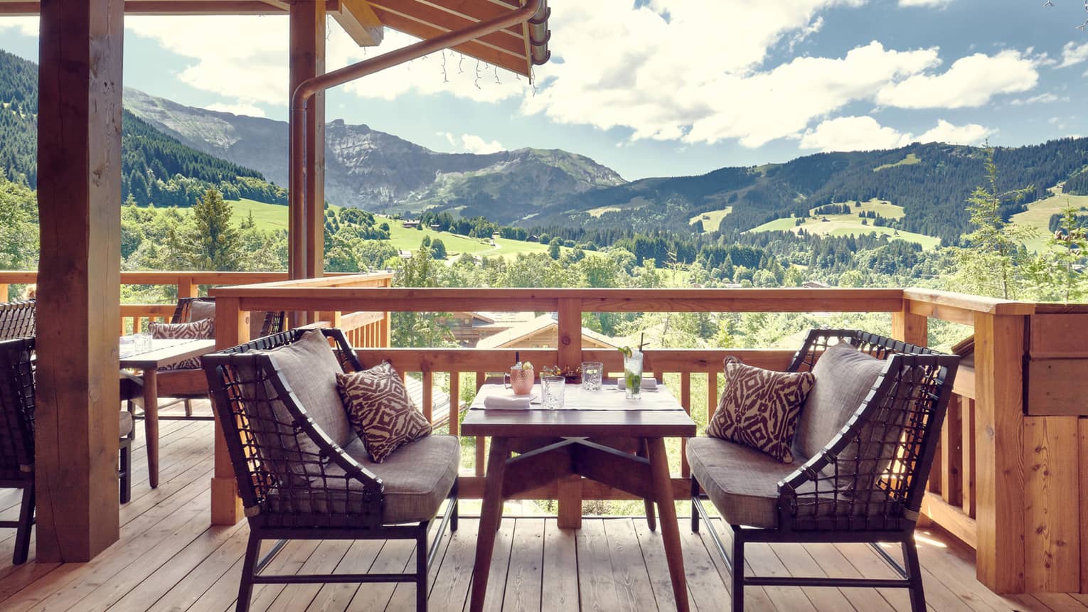 Two cushioned benches with table in middle on wooden terrace with mountain views