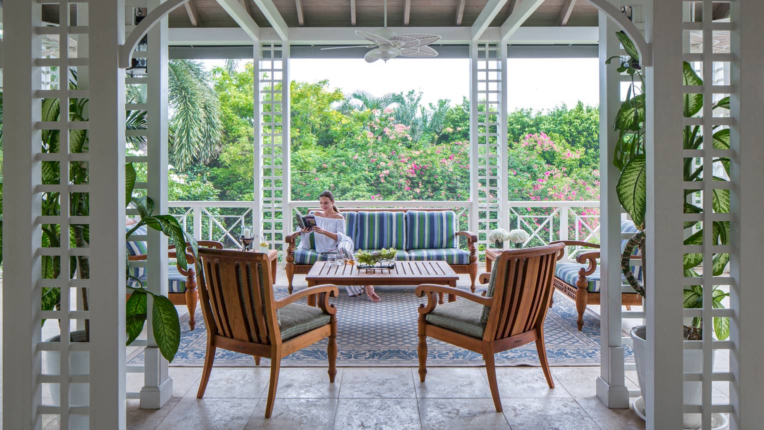 Woman reads book on plush patio sofa by chairs under awning