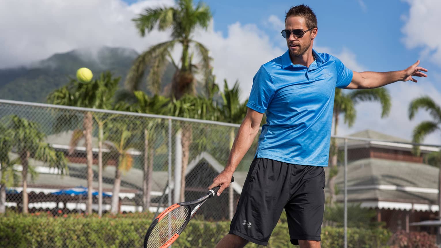 Tennis ball in air, man swings racket on court.