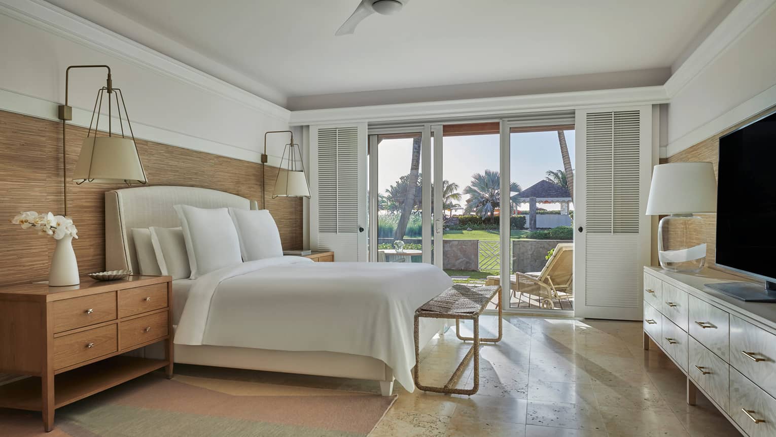 Room with king bed, tan floors, wood side tables, walk-out patio