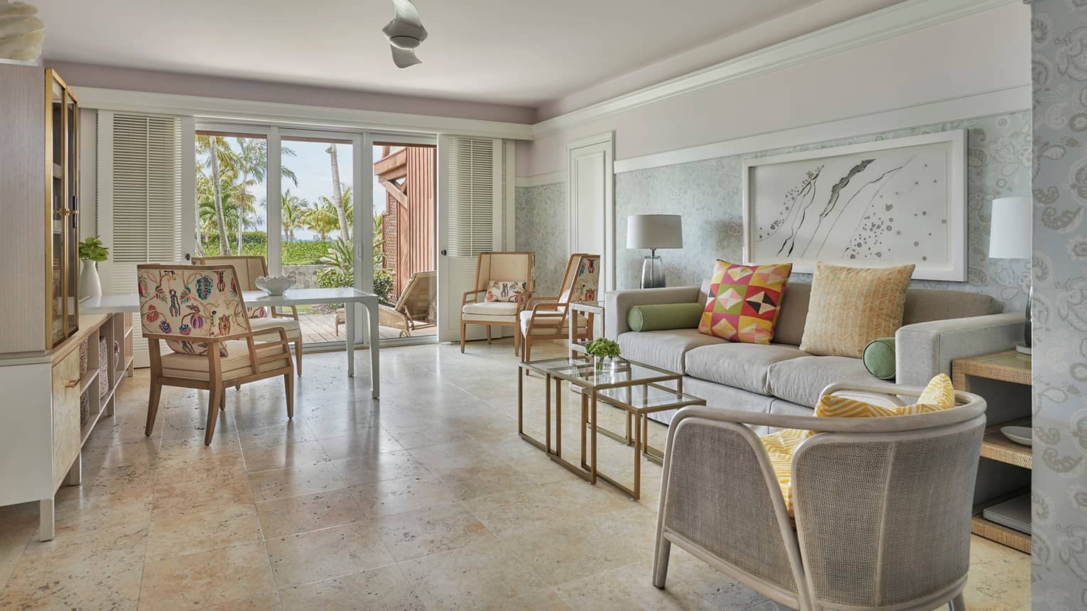 Airy living room, with tan floors, light grey sofa, arm chair, walk-out patio