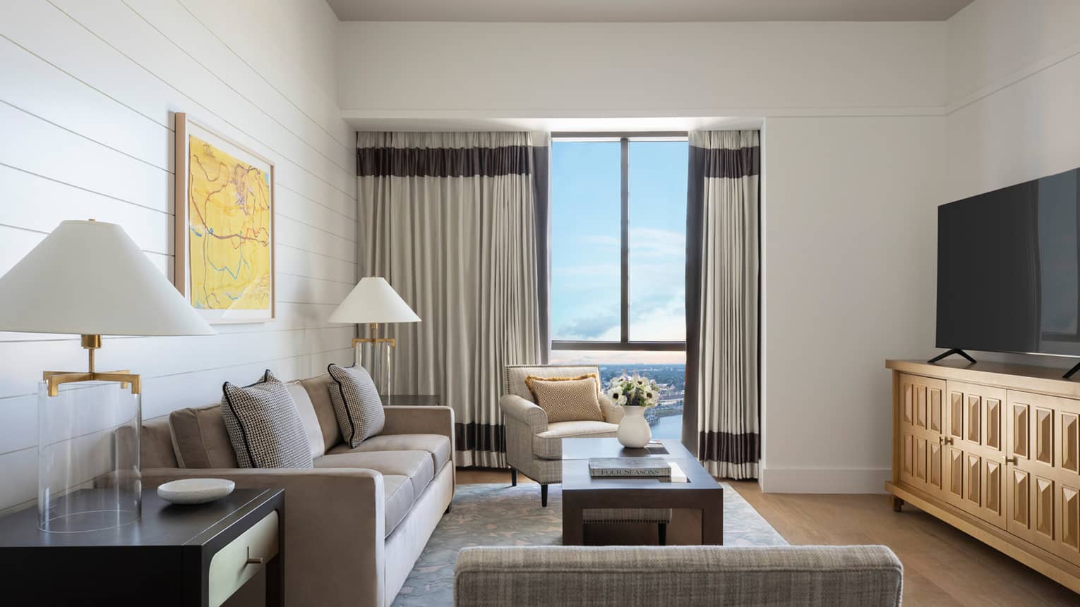 Living room with grey sofa, arm chair, TV, glass table lamps and windows