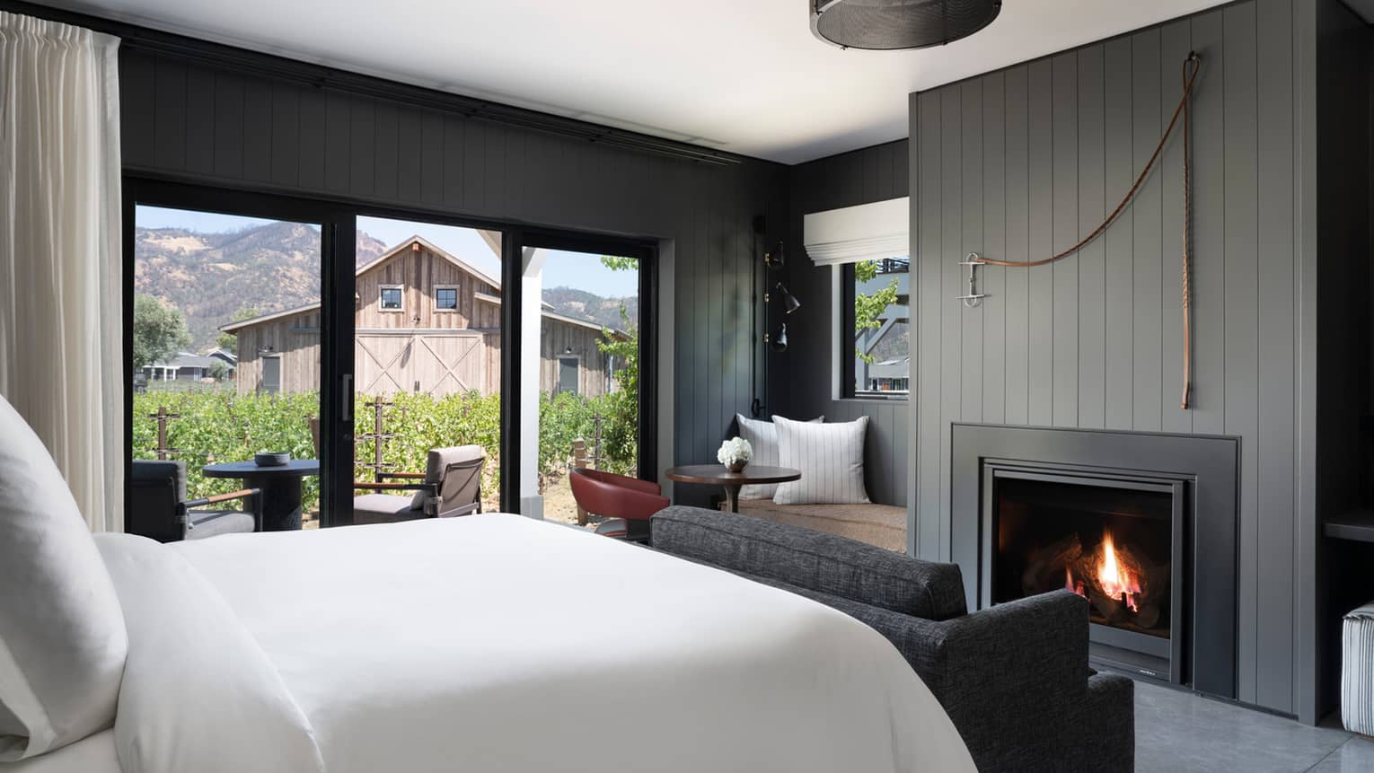 Luxury resort room with a king bed, cozy fireplace, vineyard view, seating area and outdoor patio facing rustic barn and mountains