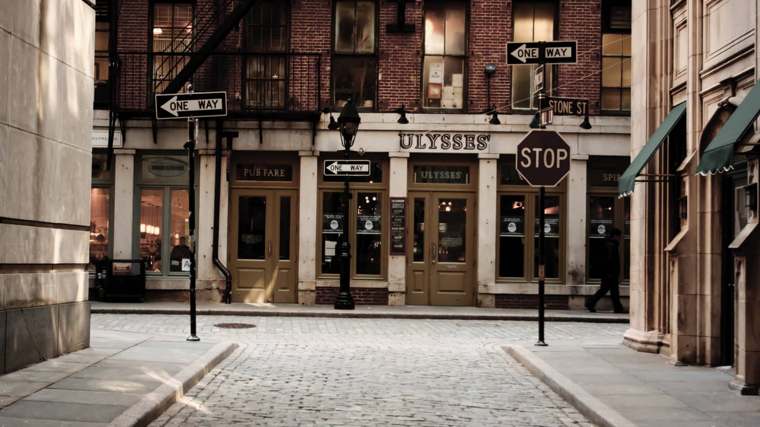 Street signs on small cobblestone road outside Ulysses pub storefront