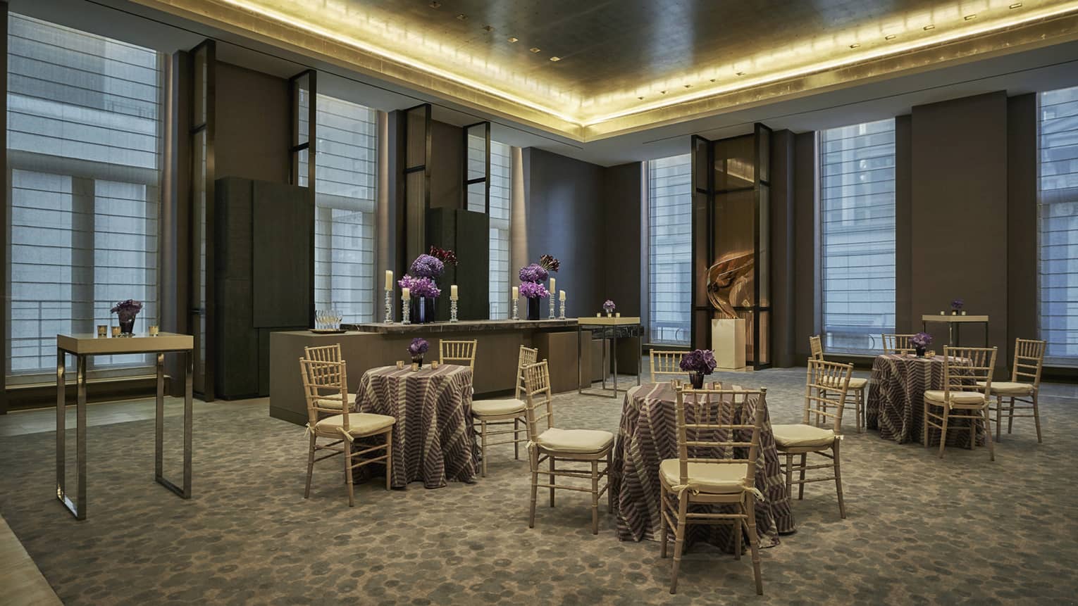 brown venue with small round tables with chairs set with purple flower arrangements