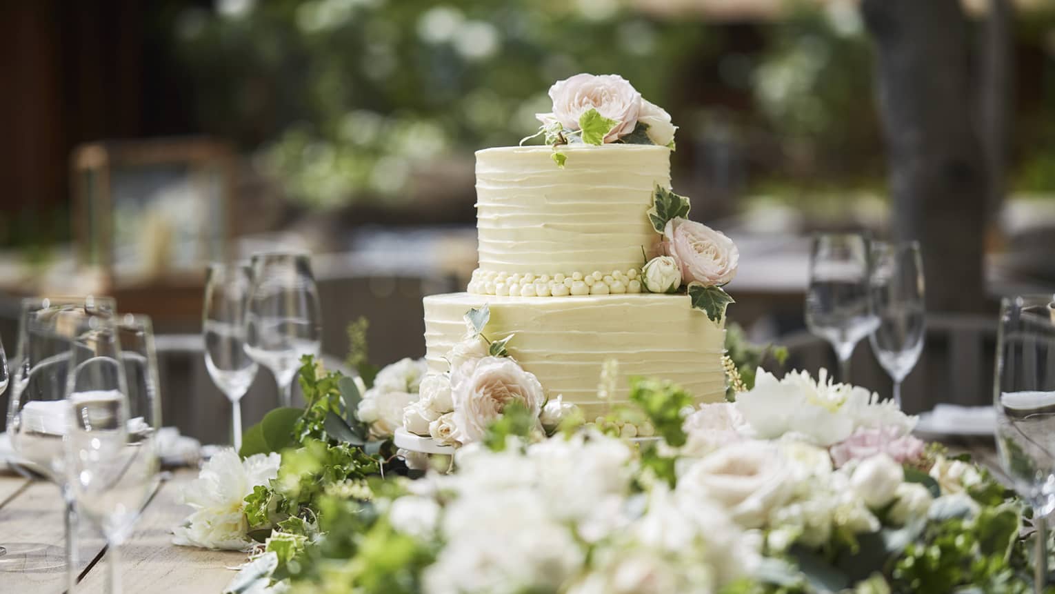 Two-tiered white wedding cake on banquet table with wine glasses, flowers