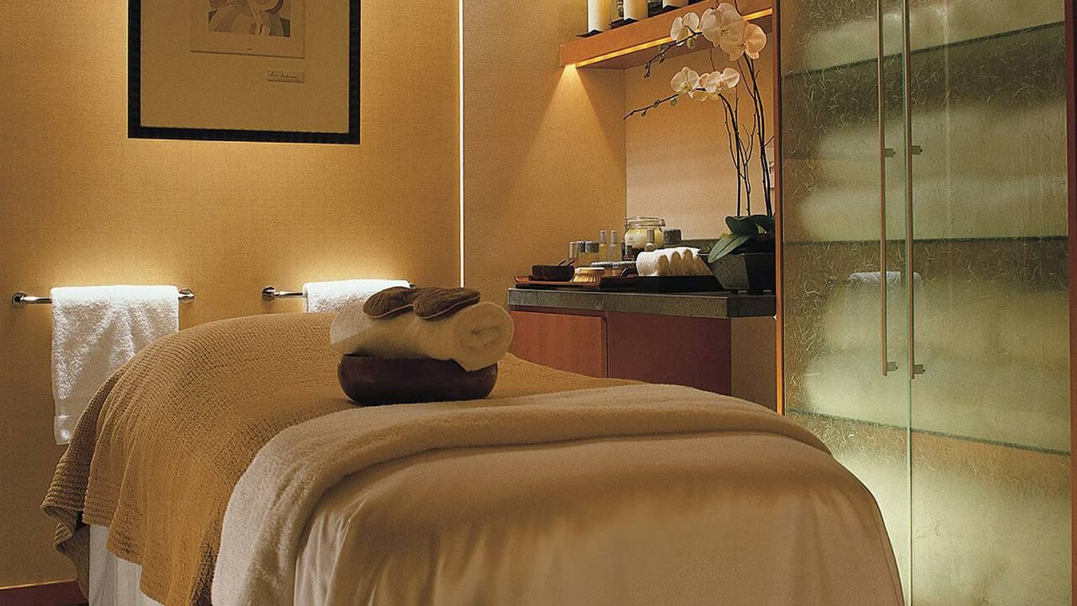 Rolled towels on massage bed in dimly-lit spa treatment room