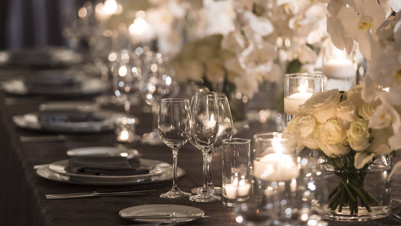 Dining table with glassware, glowing candles and white roses