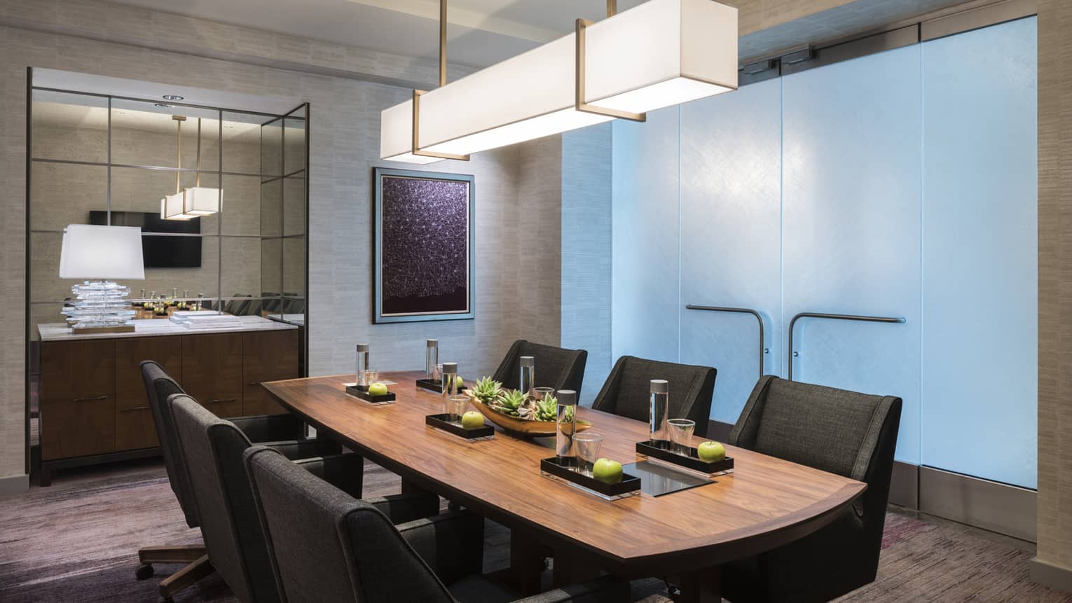 Wood boardroom meeting table with black executive chairs under modern light, glass wall