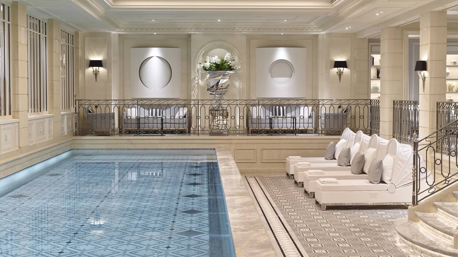 Long blue indoor swimming pool with large tile deck, steps, white lounge chairs