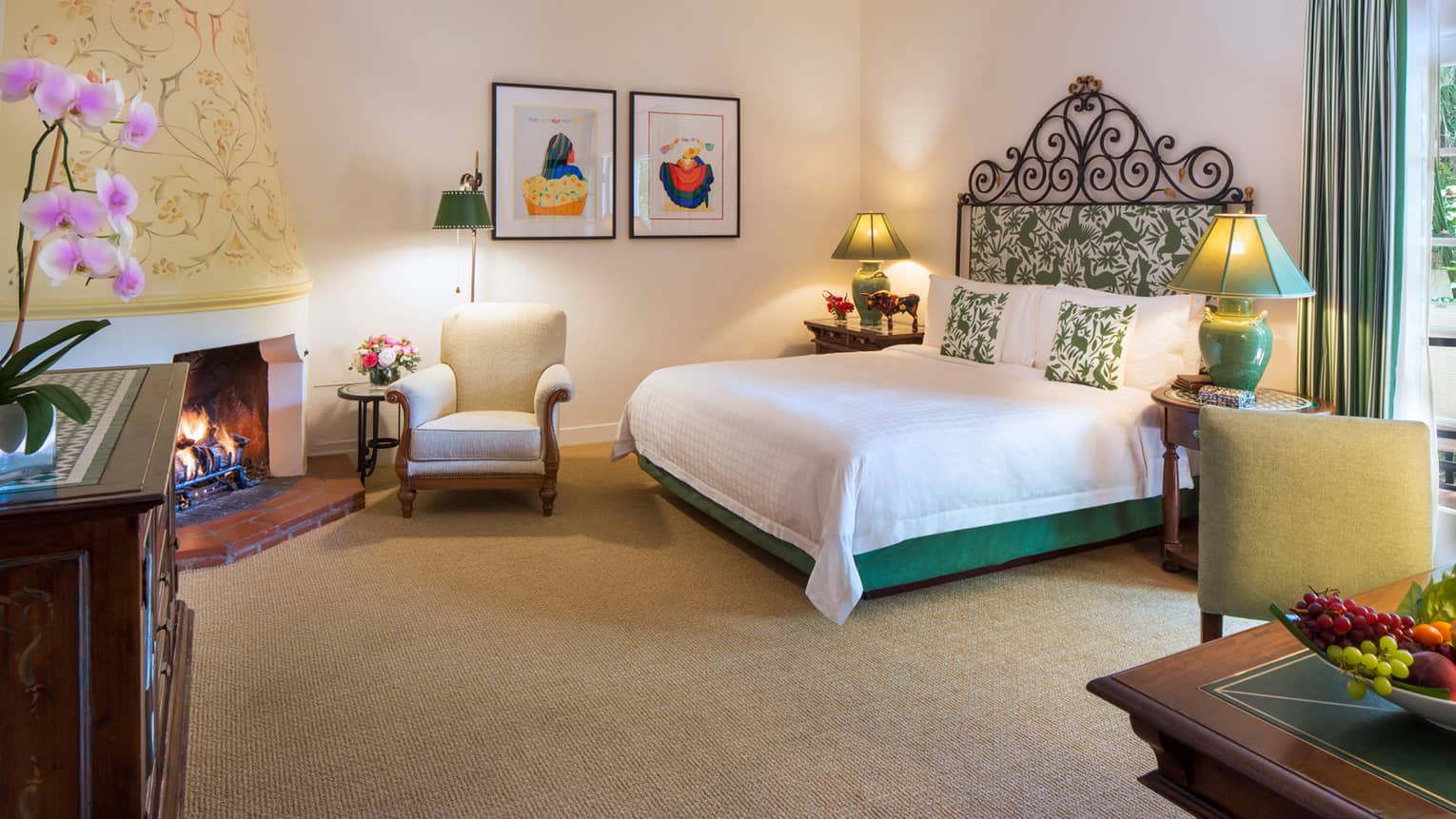 Jungle Room bed with iron and green-padded headboard, white armchair by fireplace, desk, fruit bowl