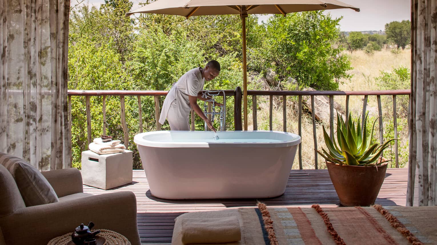 Woman draws bath in freestanding tub on patio beside large cactus plant in pot