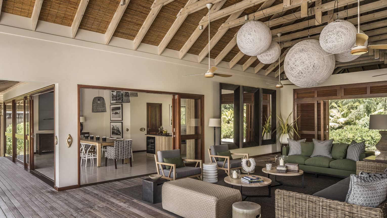 Large wicker globe chandeliers hang from beamed roof over open-air living room