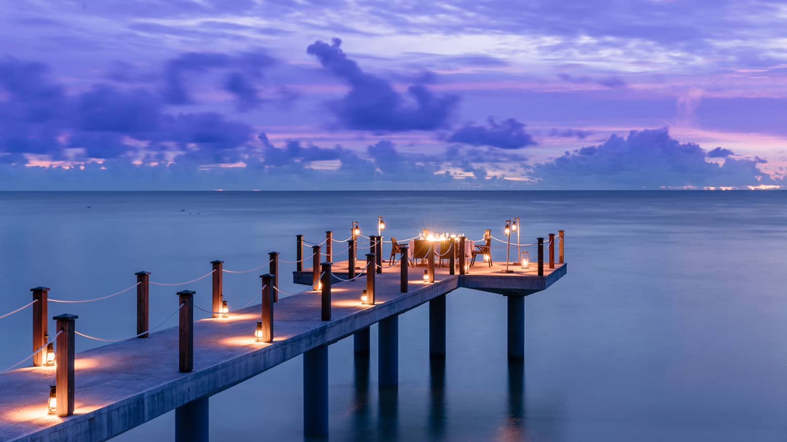 Candlelit jetty off Desroches Island with purple sunset hues