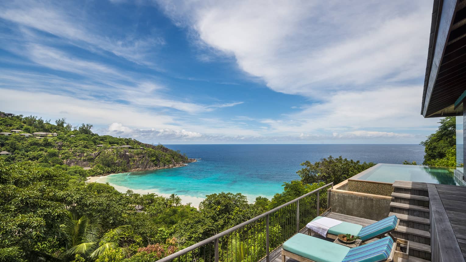 Blue lounge chairs on balcony overlooking lush mountain, beach, ocean, blue sky