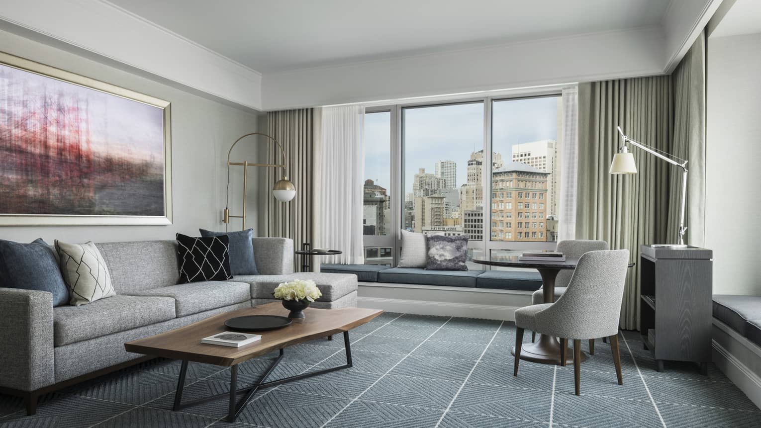 Hotel room with modern seating area, grey sofa by large window with padded bench