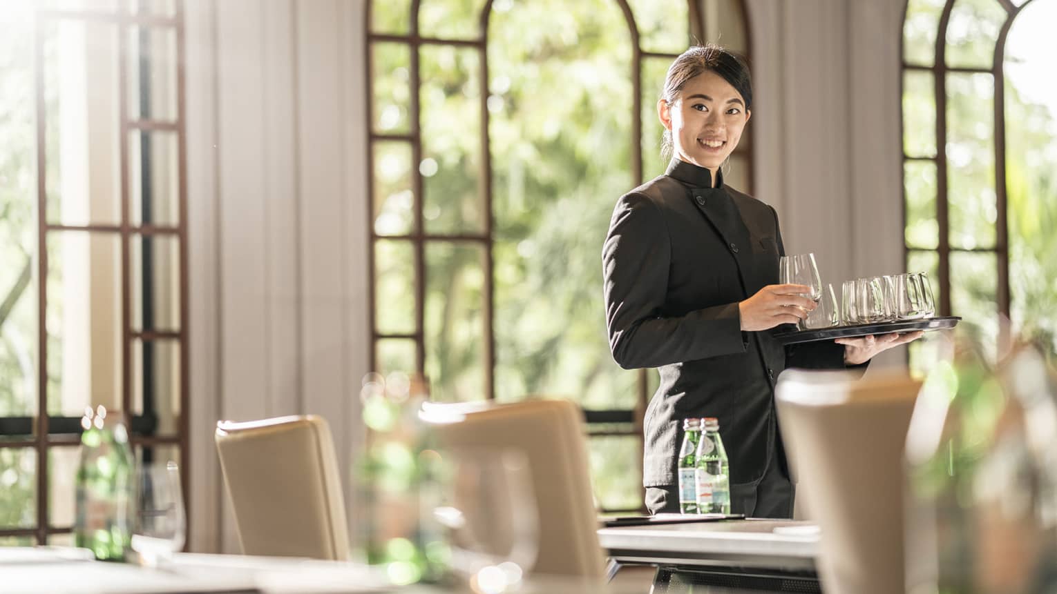 A female employee places glasses onto tables as she prepares the room for a meeting