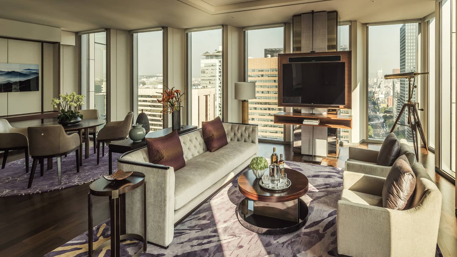Ambassador One-Bedroom Suite long sofa, brown silk pillows, two armchairs around table with liquor, corner windows and telescope