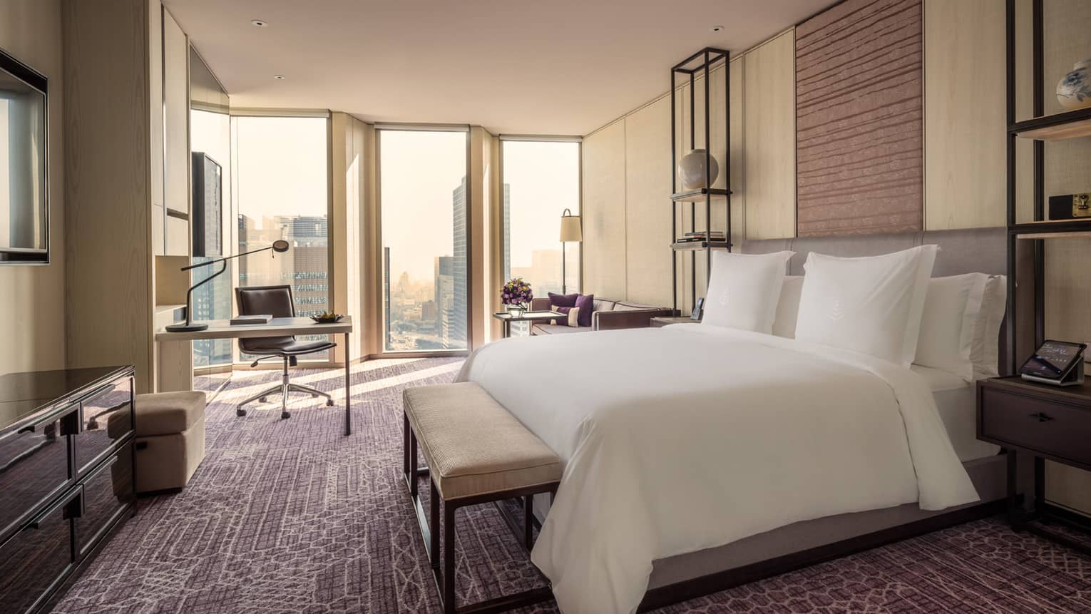 Hotel room bed with bench by work desk, chair near floor-to-ceiling windows