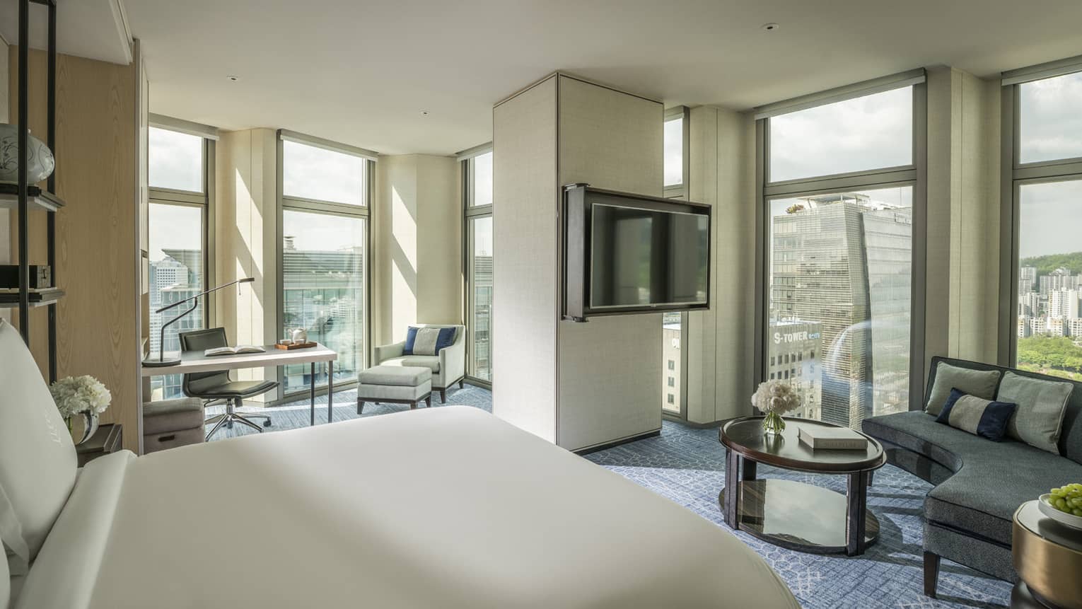 Corner Premier Room across from curved sofa by windows, TV on pillar separating work desk, armchair