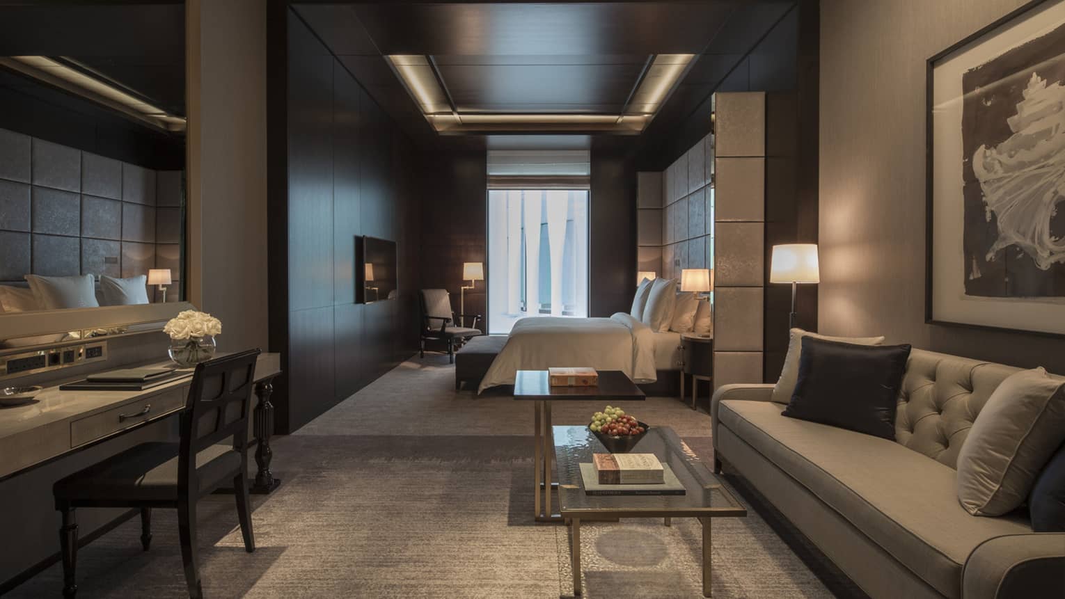 Executive room living area with full-size grey sofa and desk, bedroom in background