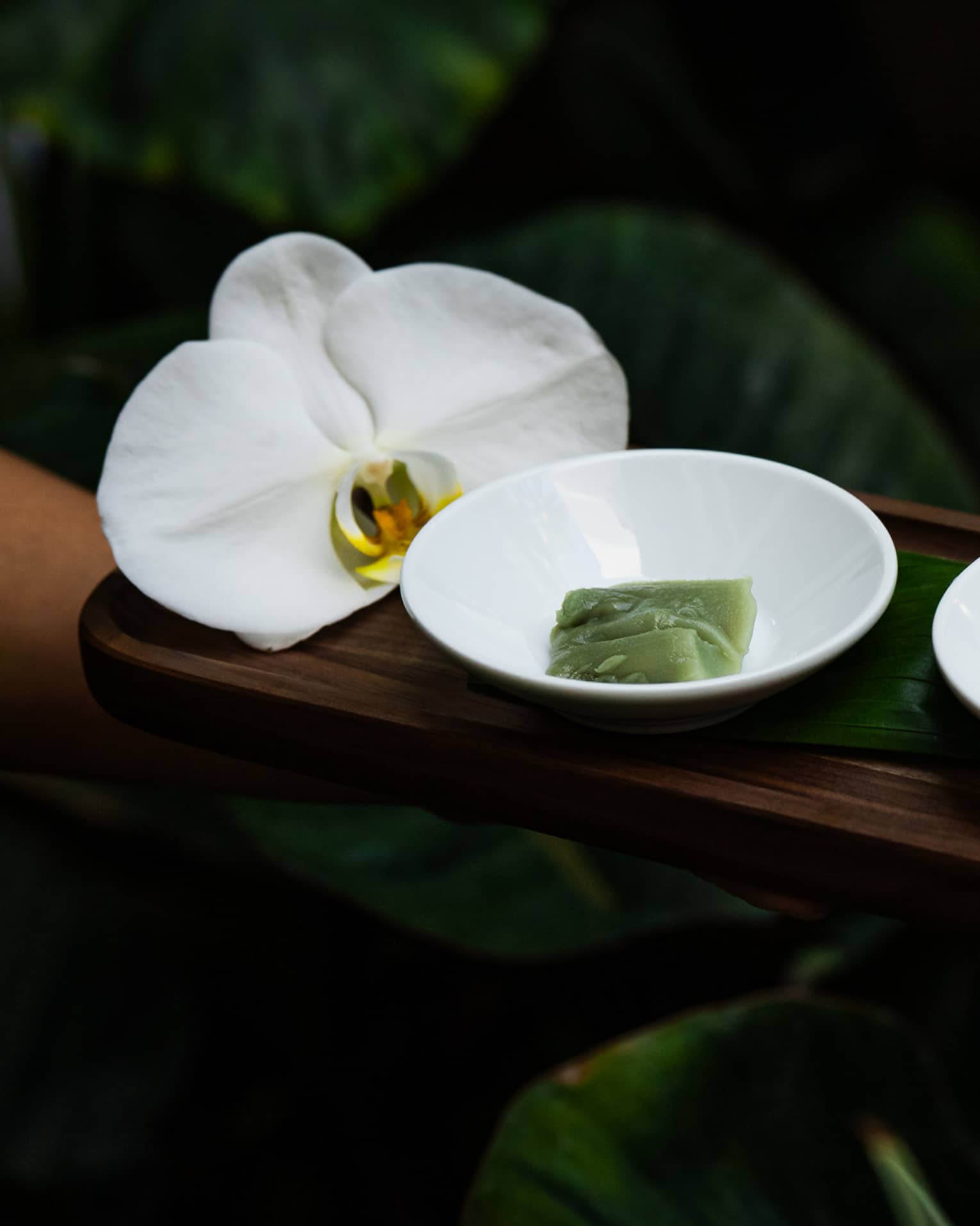 Rectangular wooden tray holds two small white bowls of spa ingredients and a large white flower