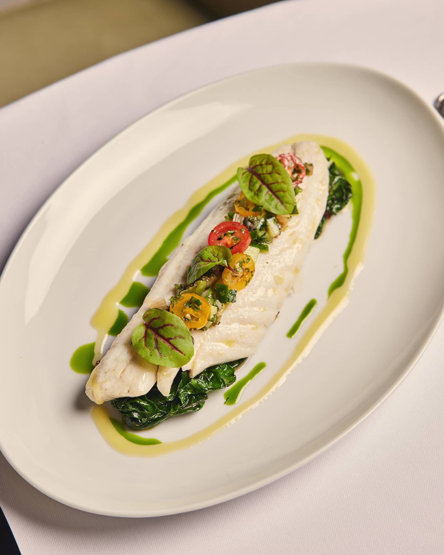 A fish dish on a green sauce with herbs and tomatos.