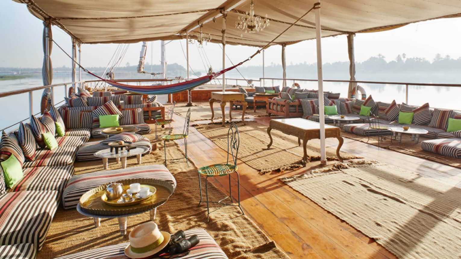 River Cruise felucca boat with wood floors, striped patio sofas and tables under canopy