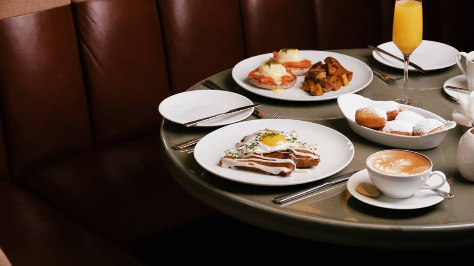 White dishes of brunch dishes and mimosa flute on round grey table