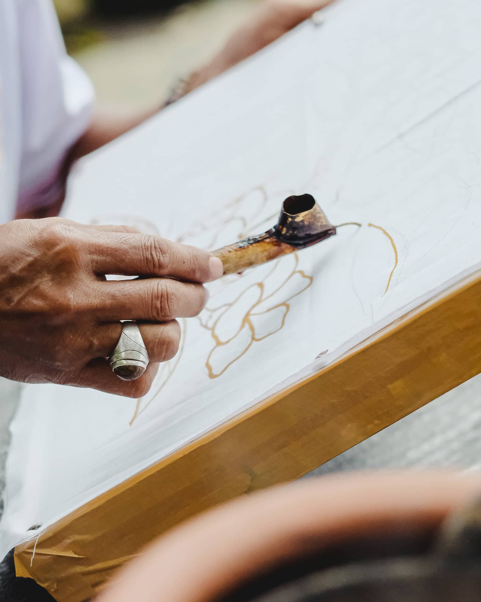 Close-up of someone using a metal Canting pen to draw a pattern in wax on a flat canvas. 