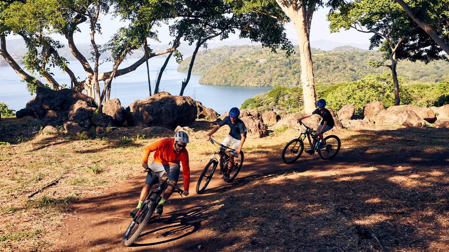 Three people on mountain bikes on a trail overlooking water and mountains