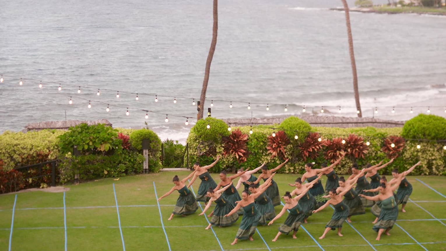 A group of hula dancers perform on an oceanside lawn at luxury resort