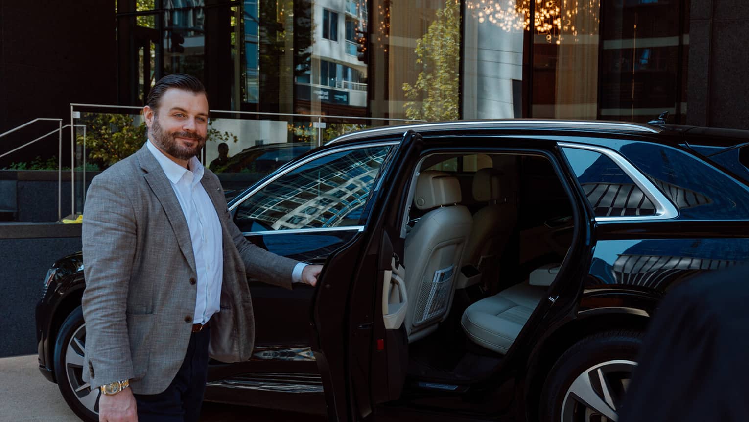 A man holds the door of a black SUV open in front of hotel entrance