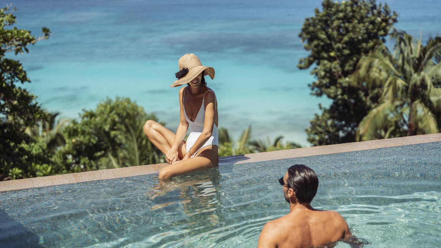 A couple relaxes in an infinity pool overlooking the beach