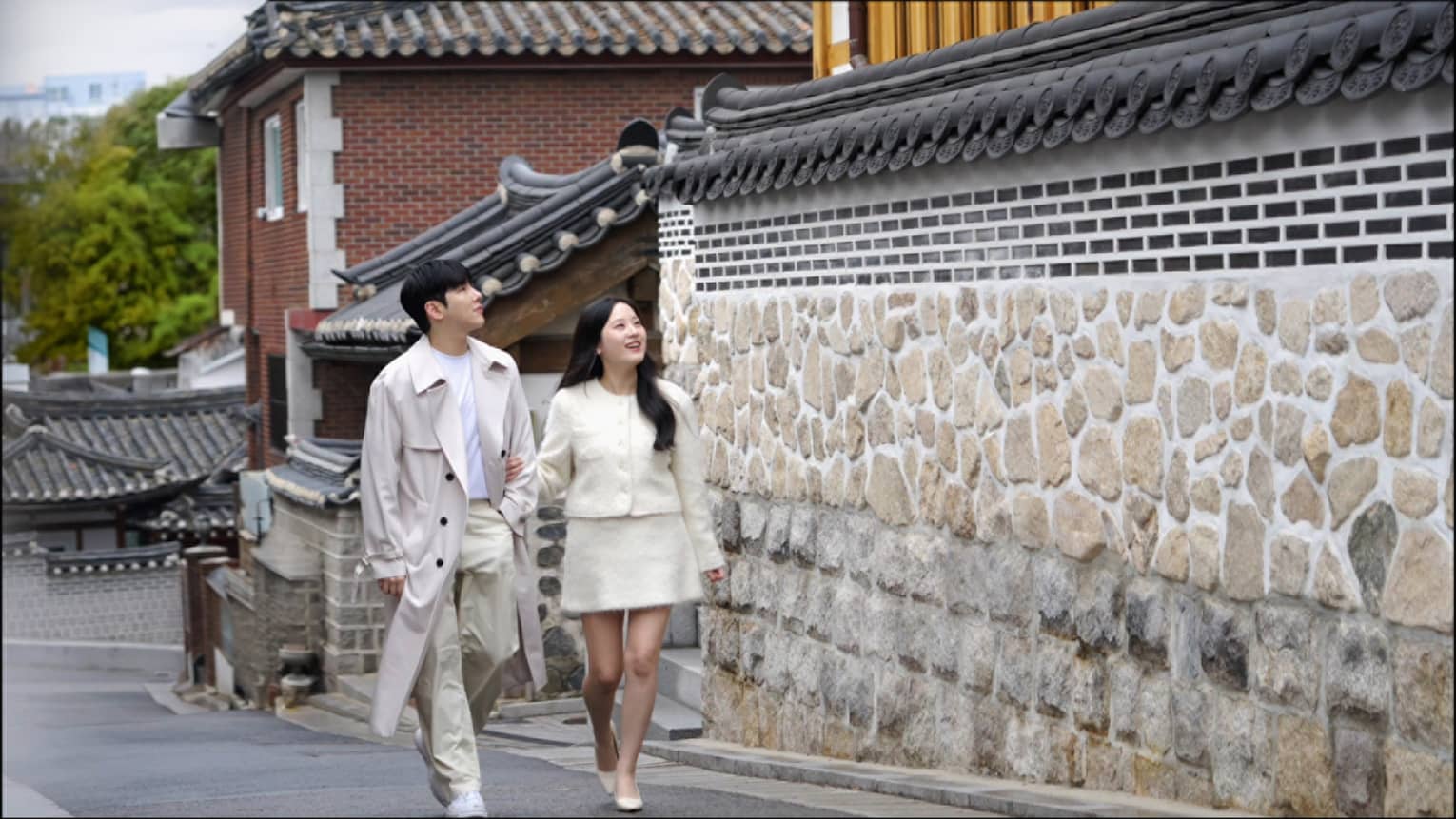Smiling couple walks together along tall stone wall
