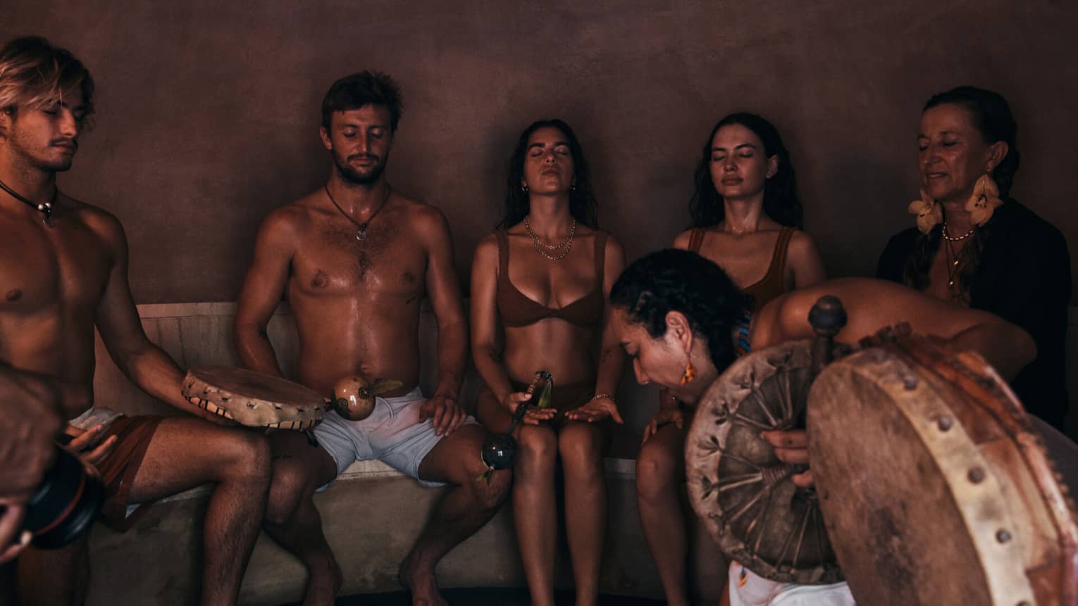 Group of people sitting side-by-side with their eyes closed and holding a drum.