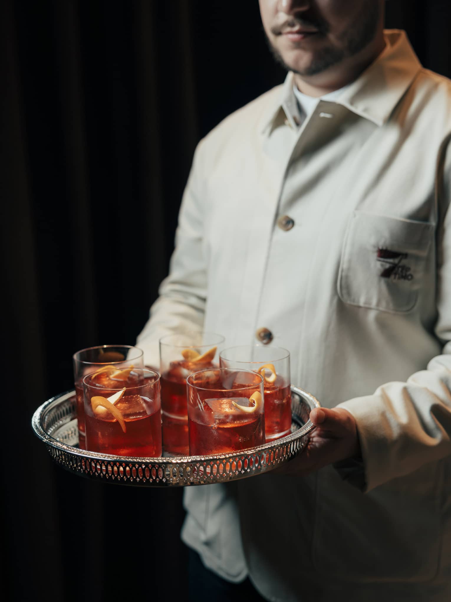 Bartender carries a silver tray of Old Fashioned cocktails