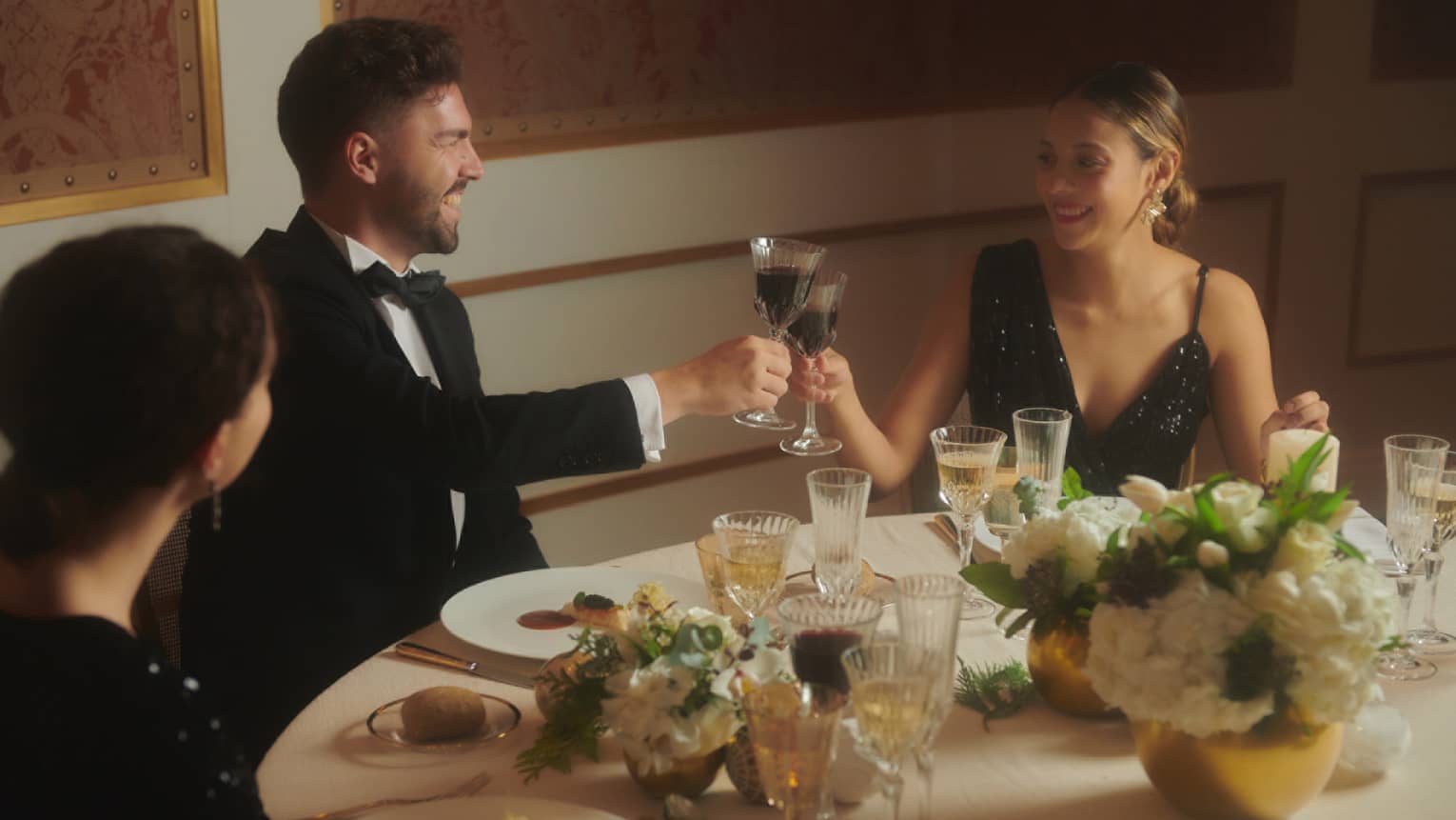 Three people toasting with wine while waring fine clothing.