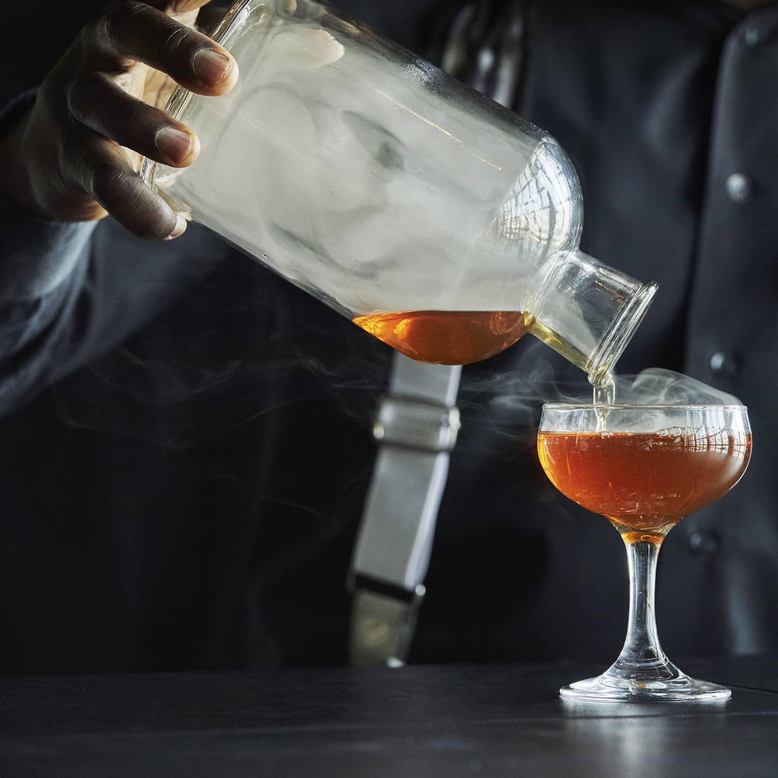 Smoke rolls off the decanter as a Four Seasons staff member pours bourbon into a coupe glass