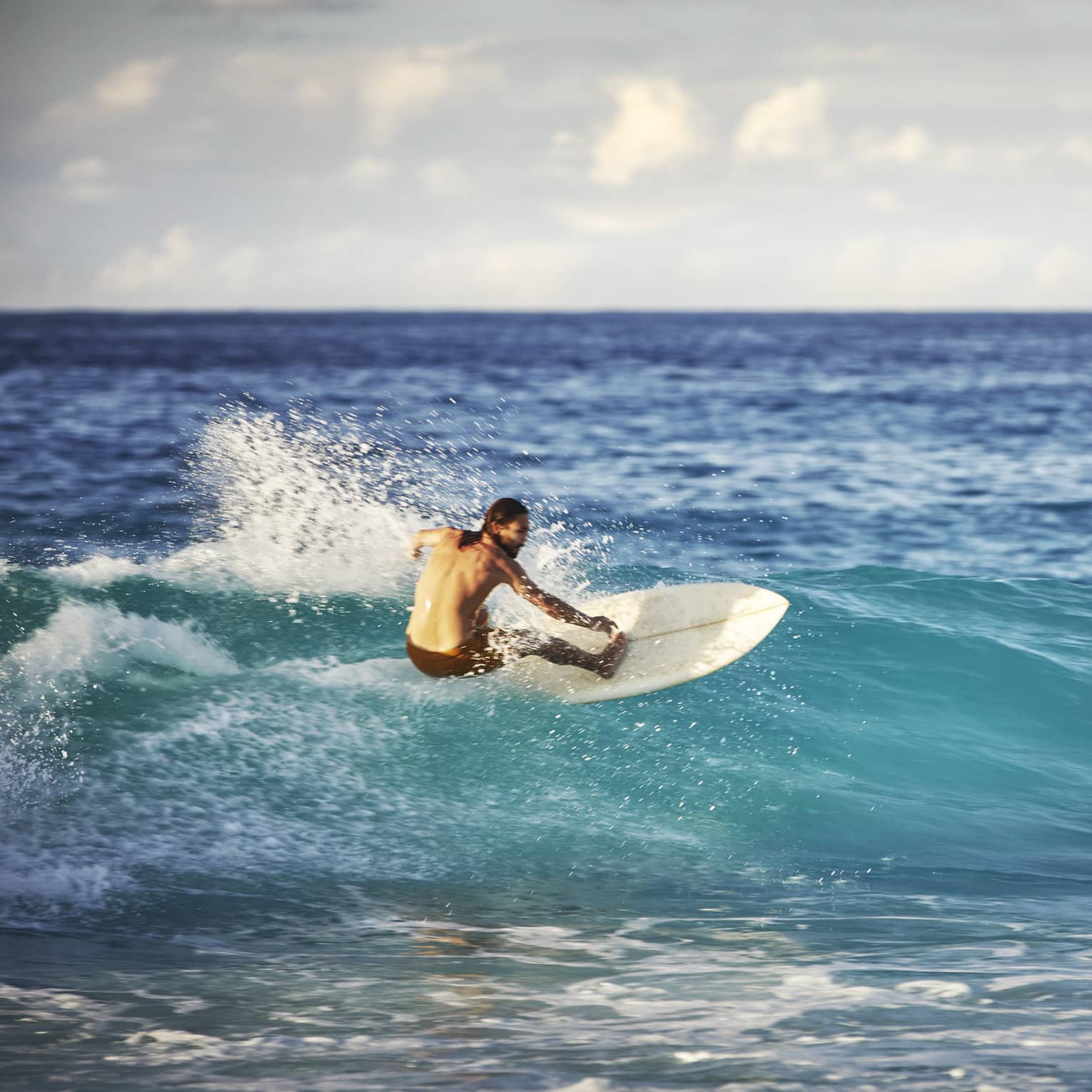 On an expanse of water, a surfer leans back on his board and surfs the face of a wave as white water splashes up behind him.