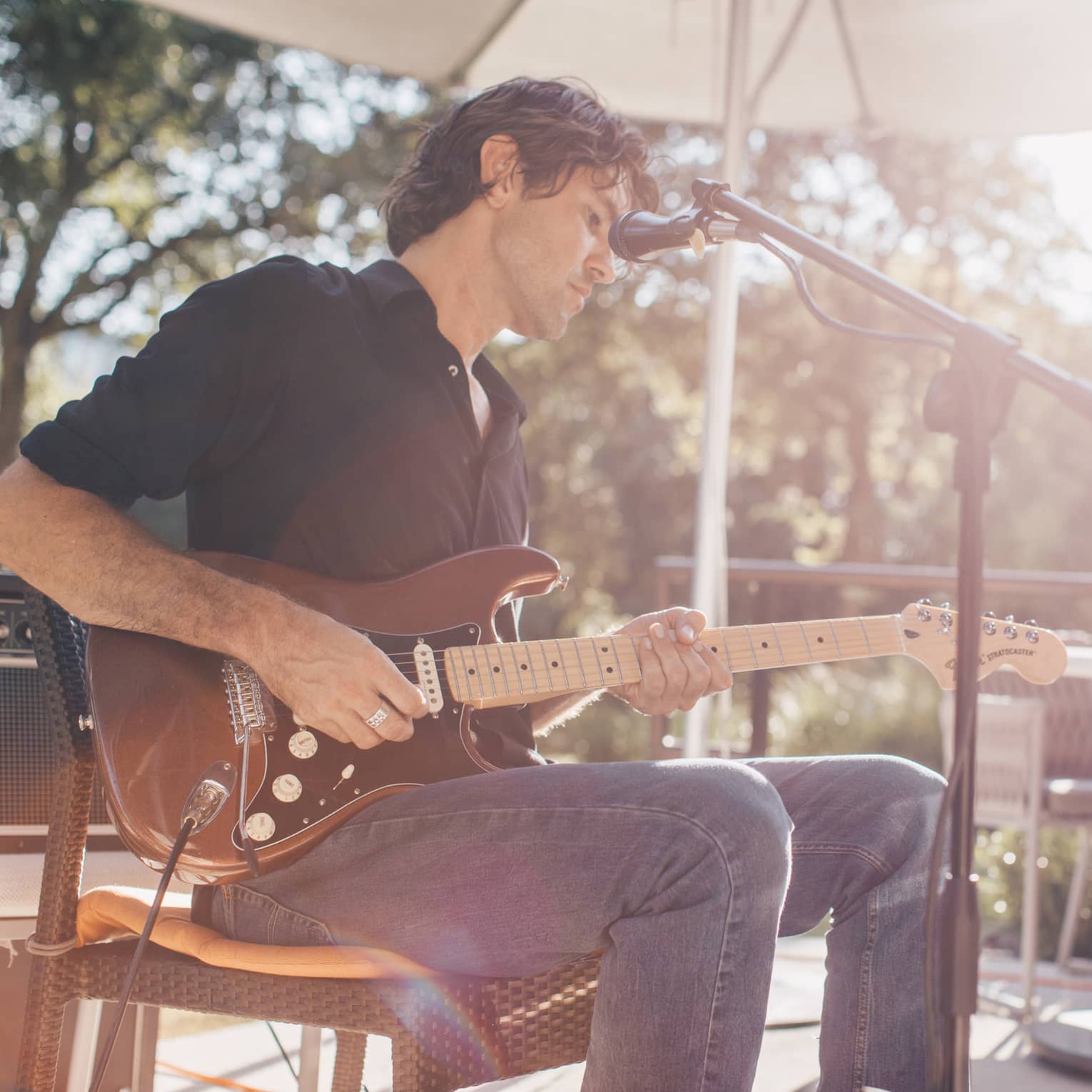Man plays electric guitar at microphone on sunny patio