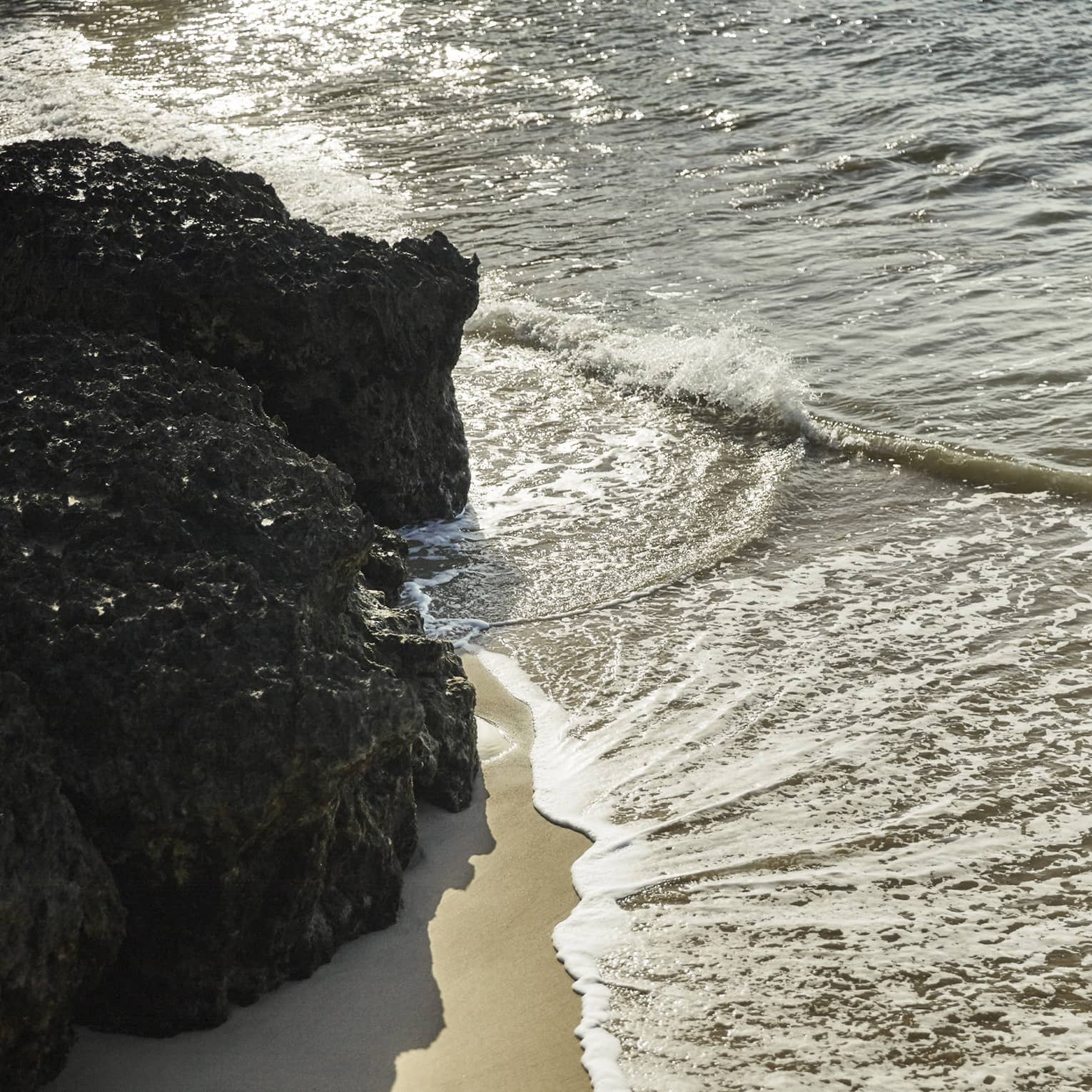Calm waves brush up against a smooth beach and nearby rock